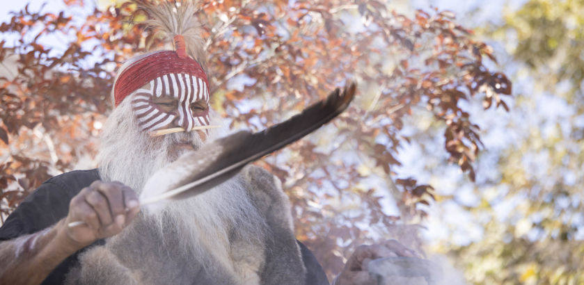 First Nations Elder outdoors holding a feather in the foreground.