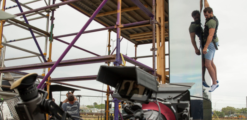 Stunt man hanging from balcony as the film crew record him. 