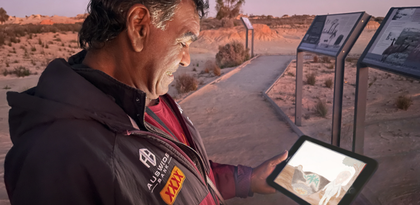 First Nations Elder standing in Mungo National Park viewing the Walk Together app on a tablet.