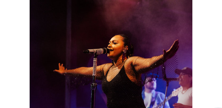 Jessica Mauboy, a First Nations woman sings into microphone on stage. 