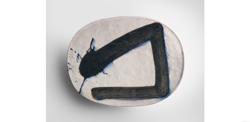 An oval ceramic piece painted with a calligraphy brushstroke sits on a white background.