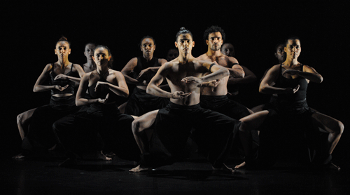 Dancers in a squatted position with there arms forming a circle in front of them.