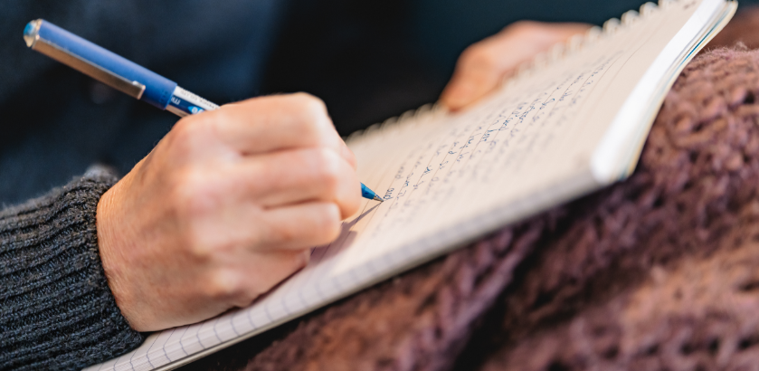 Close up of a hand writing with a pen on a lined notebook.