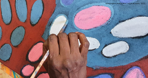 Mornington Island Arts’ artist’s hand holding a paintbrush working on a painting.