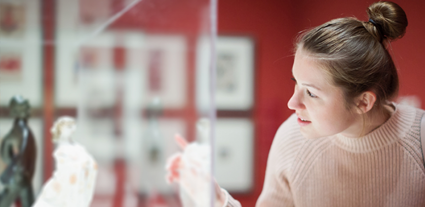 A woman peers into a cabinet with a statue inside. 