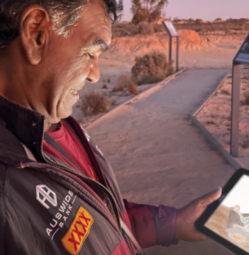 First Nations Elder standing in Mungo National Park viewing the Walk Together app on a tablet.