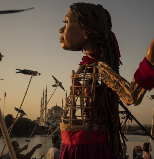 A large animatronic puppet walks through excited crowds on a bridge.