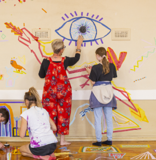 A woman and three teenagers creating art on the wall and floor using colourful tape.