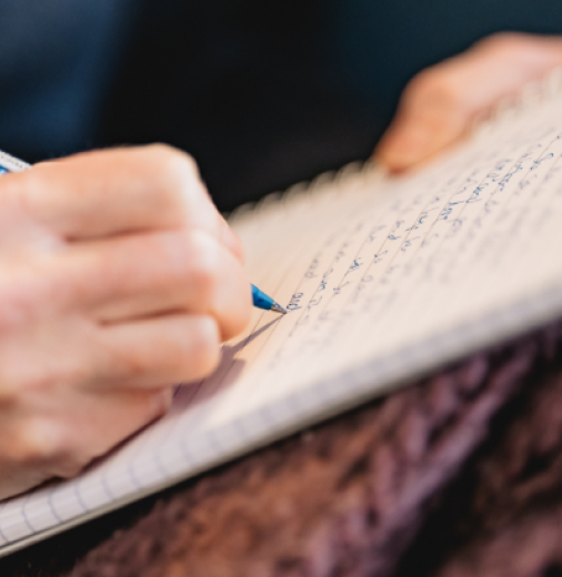 Close up of a hand writing with a pen on a lined notebook.