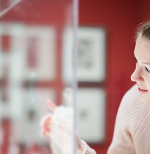 A woman peers into a cabinet with a statue inside. 