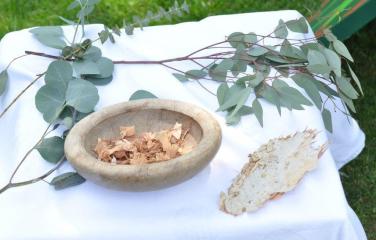 A First Nations ceremonial wooden bowl sits on a table surrounded by eucalyptus leaves. 