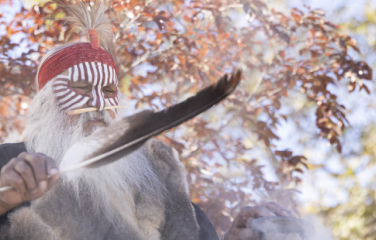 First Nations Elder outdoors holding a feather in the foreground.