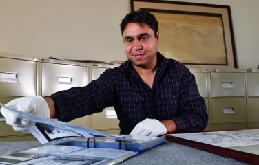 First Nations male heritage officers examines a folio of photos wearing gloves. 